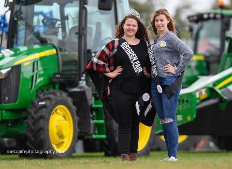 Melody Riedl and Emma Wheeler standing in front of a John Deere tractor